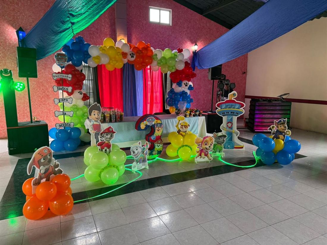 Montaje de una fiesta infantil temática con arco de globos de colores y figuras de caricatura sobre la pista.