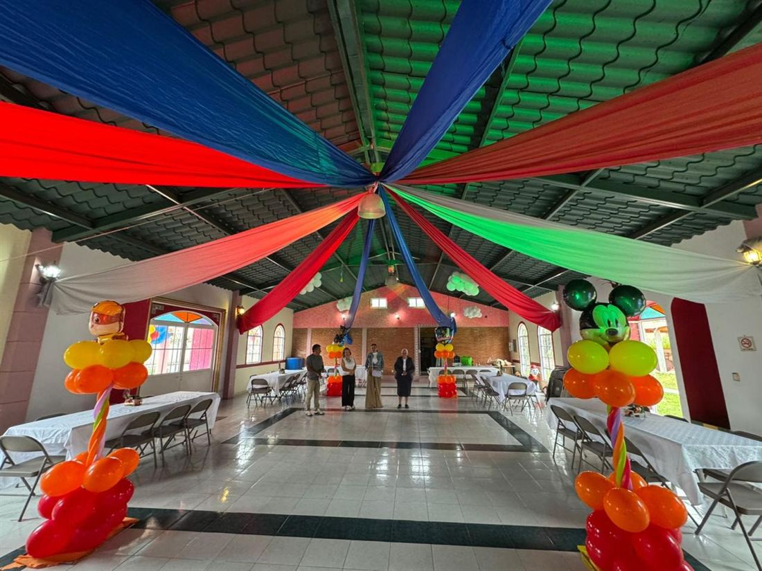 Vista a lo largo del salón con telas de colores tendidas desde el centro del techo, mesas a los costados y la pista despejada al centro.